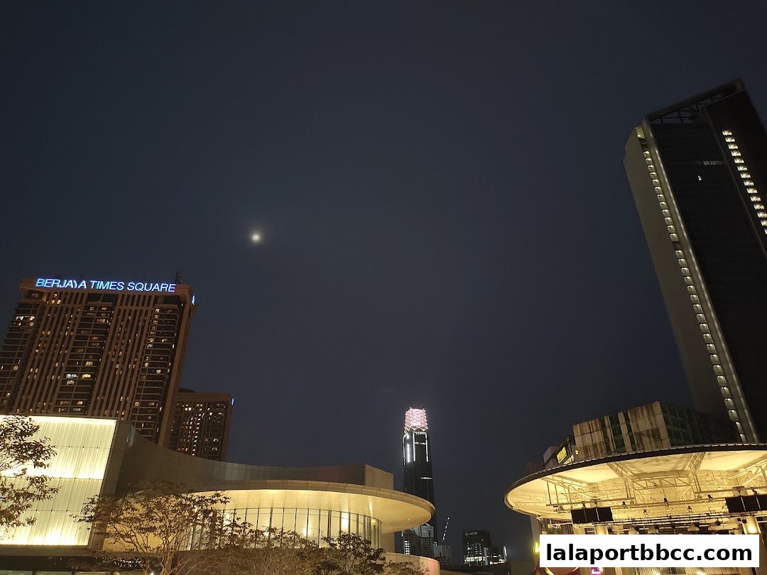 Night view of city skyline with illuminated buildings and a crescent moon.