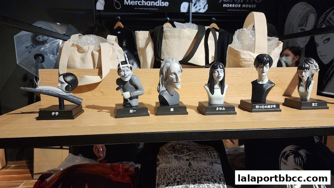Display of Junji Ito character busts and merchandise, including bags and apparel.