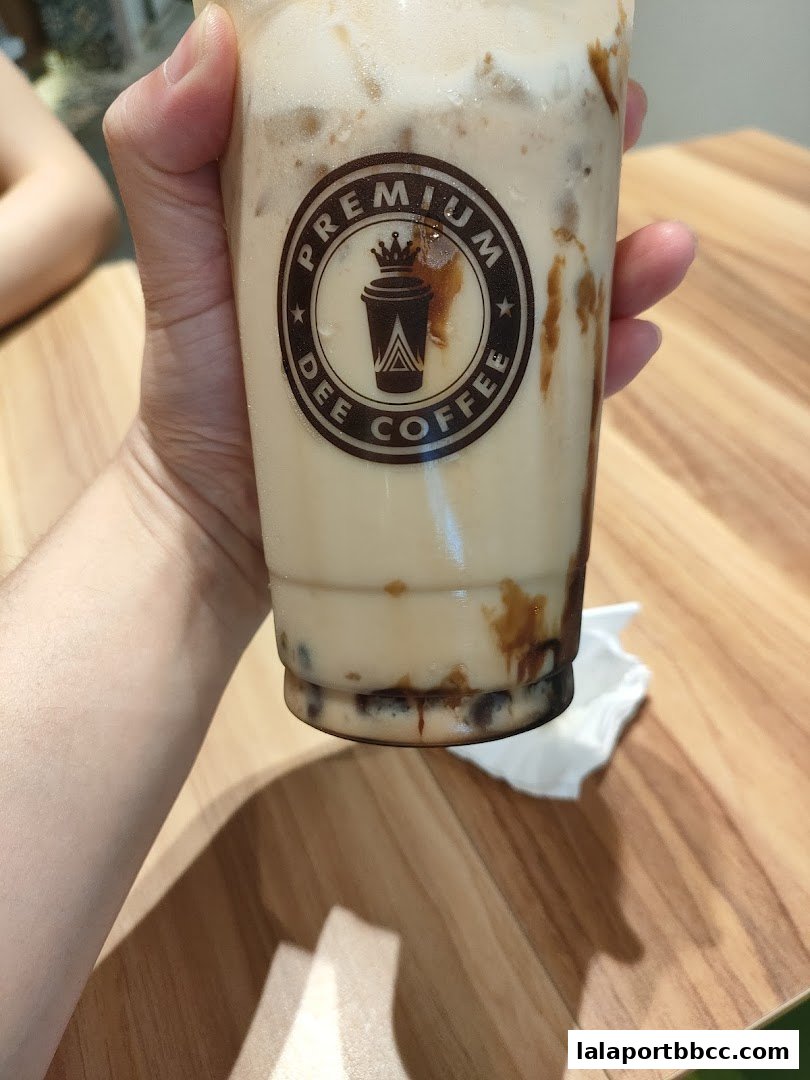 A hand holds a large iced coffee drink with the Dee Coffee logo visible.