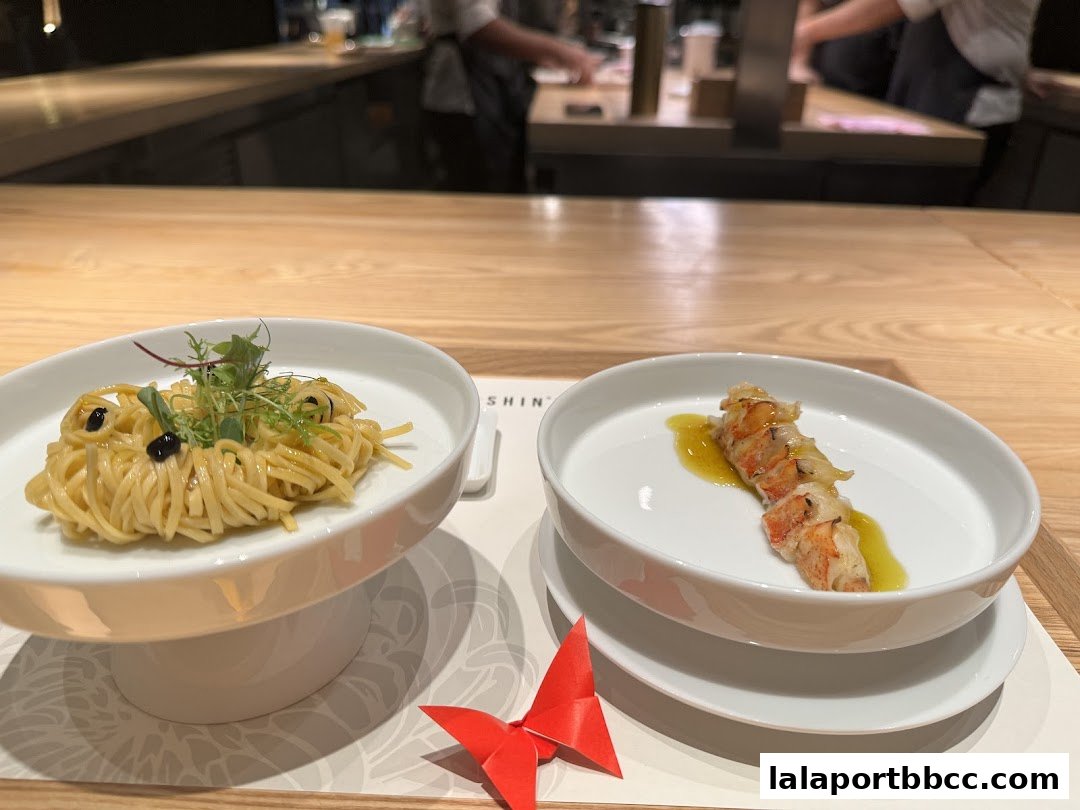 Two elegantly presented dishes, one with pasta and greens, the other with lobster, at ShinLabo by James Won.