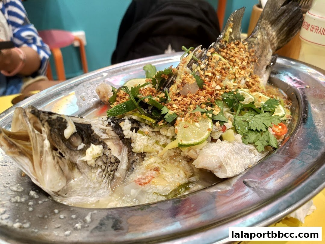 A whole steamed fish dish with lime, cilantro, and crispy garlic served on a metal platter.
