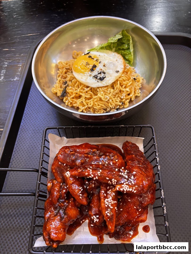 A bowl of instant noodles topped with a fried egg and a side of glazed chicken wings.