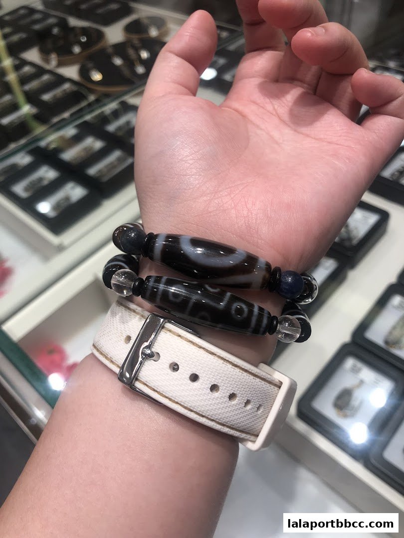 A person's wrist adorned with two Tibetan Dzi bead bracelets and a white watch.