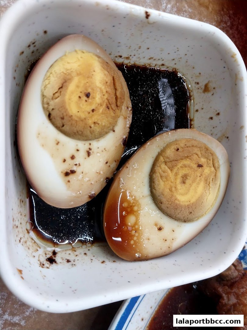 Two halves of braised eggs in a white bowl with dark sauce.