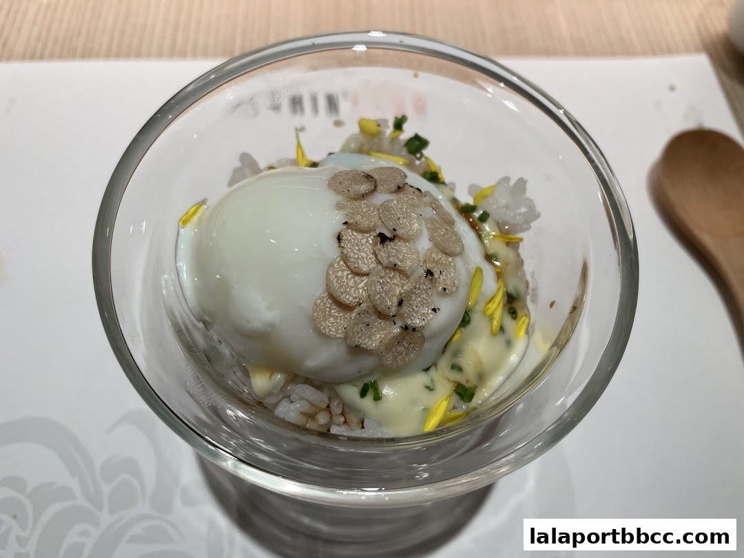 A close-up of a gourmet dish with a poached egg, rice, and truffle shavings in a glass.