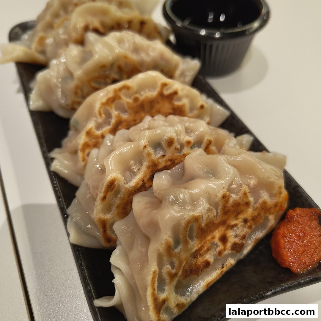 A close-up shot of pan-fried gyoza served on a black plate with dipping sauce and chili paste.