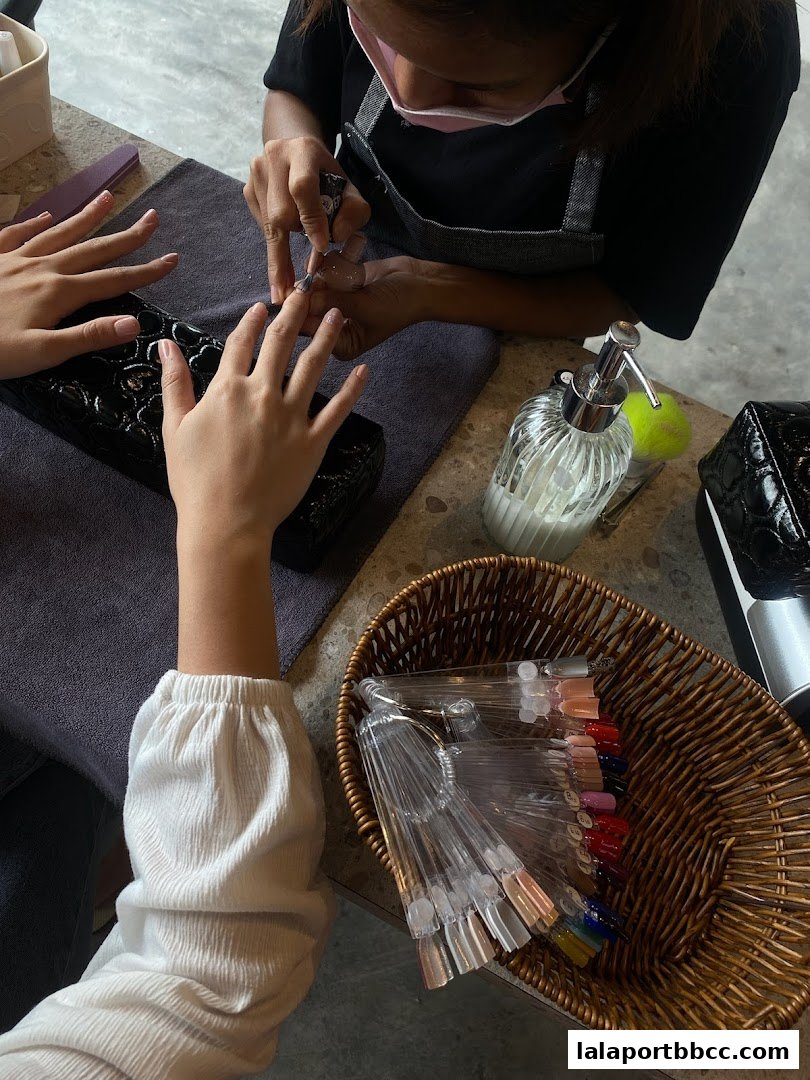 A nail technician applies polish to a client's nails, with color swatches in a basket.
