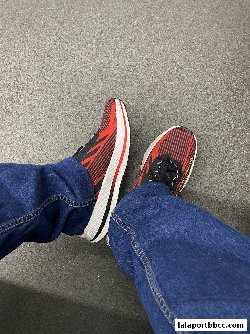 A person wearing red and black Skechers running shoes and blue jeans.