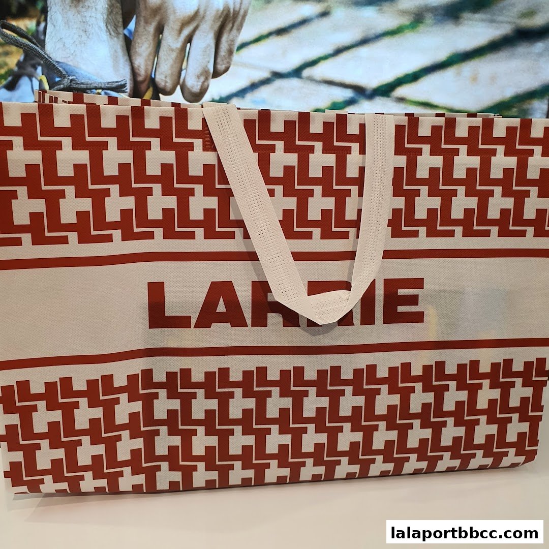 A reusable shopping bag with a red and white geometric pattern and the Larrie logo.