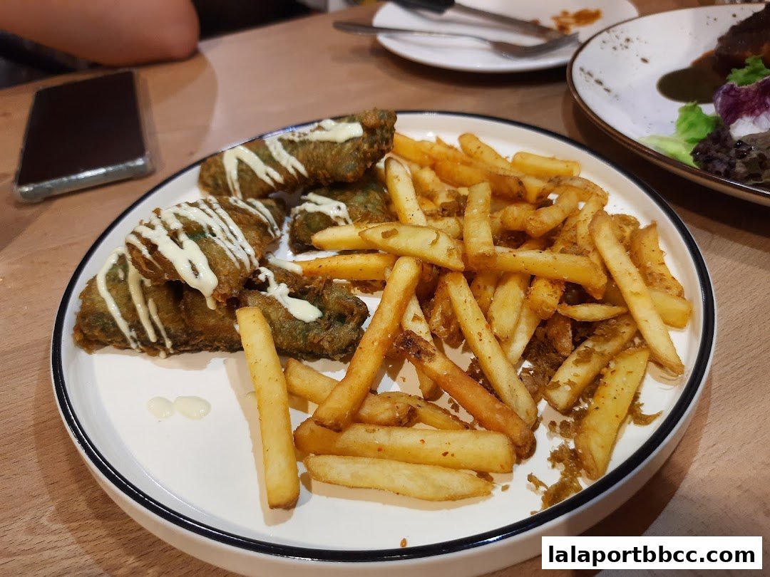 A plate of fried food, including what appears to be battered green items and french fries, is served with mayonnaise.