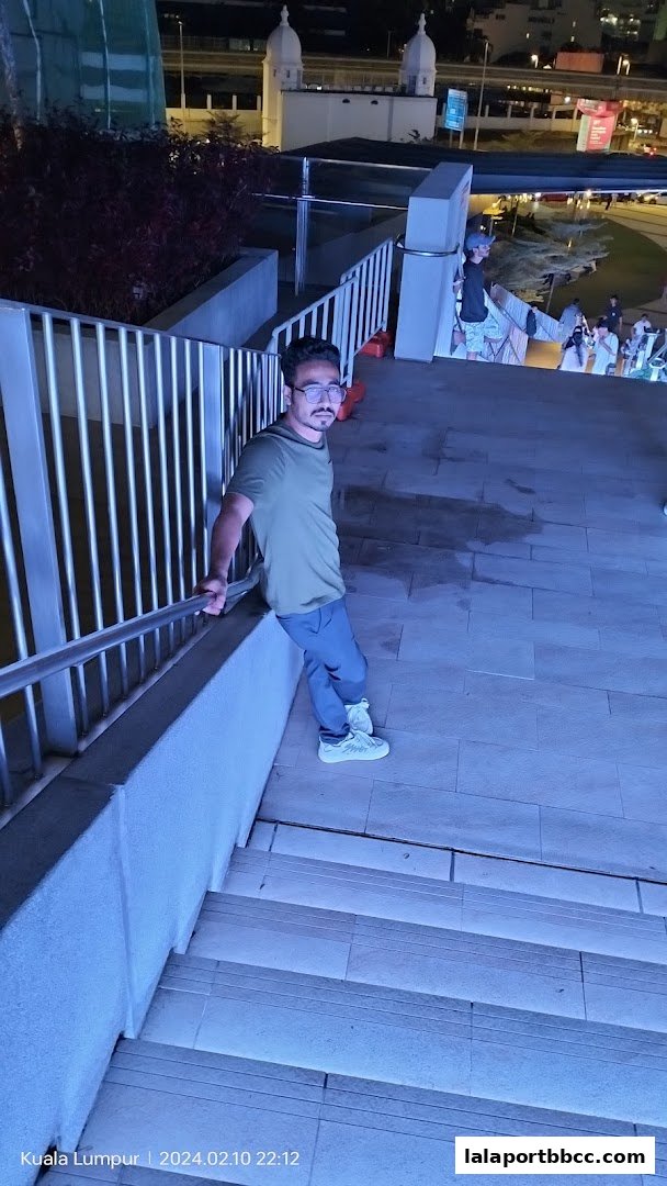 A man leans on a railing on a set of illuminated stairs at night.