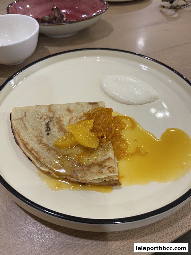 A close-up of a crepe with orange slices, syrup, and a dollop of cream.