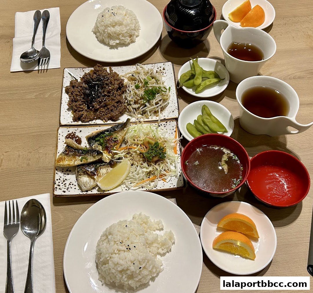 A table setting with two Japanese meals, featuring grilled fish, rice, soup, and edamame.