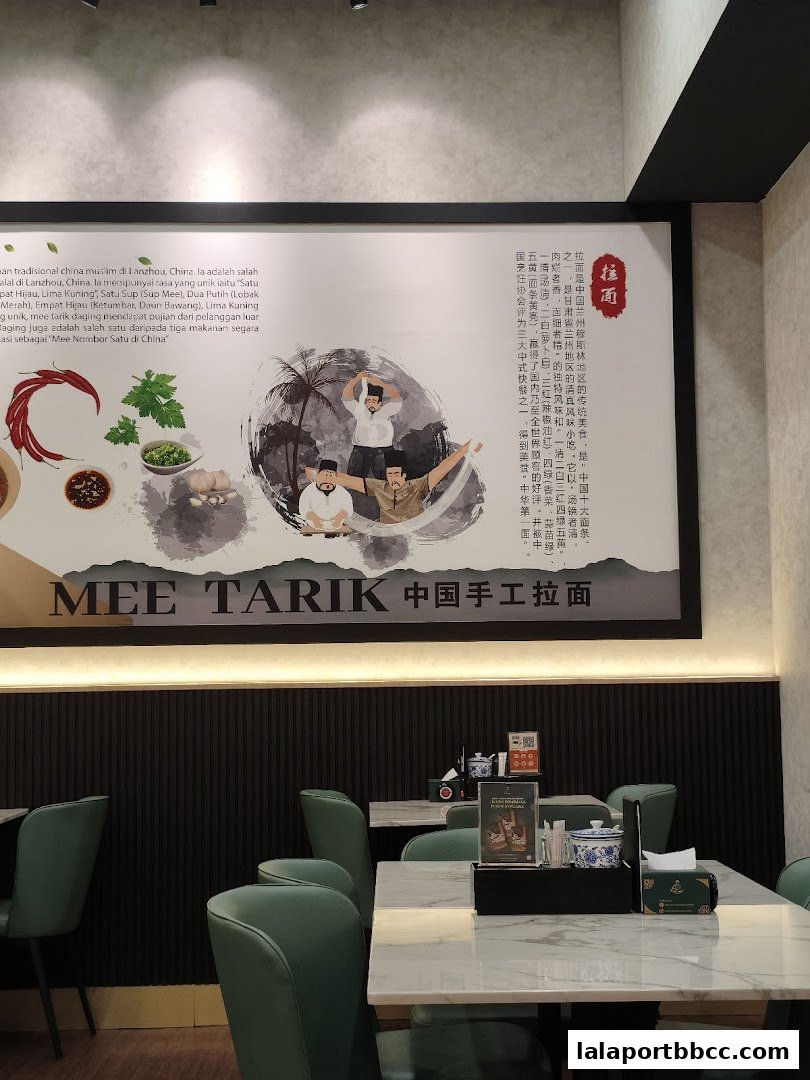 Interior of a restaurant with green chairs and tables, featuring a large mural about Mee Tarik.