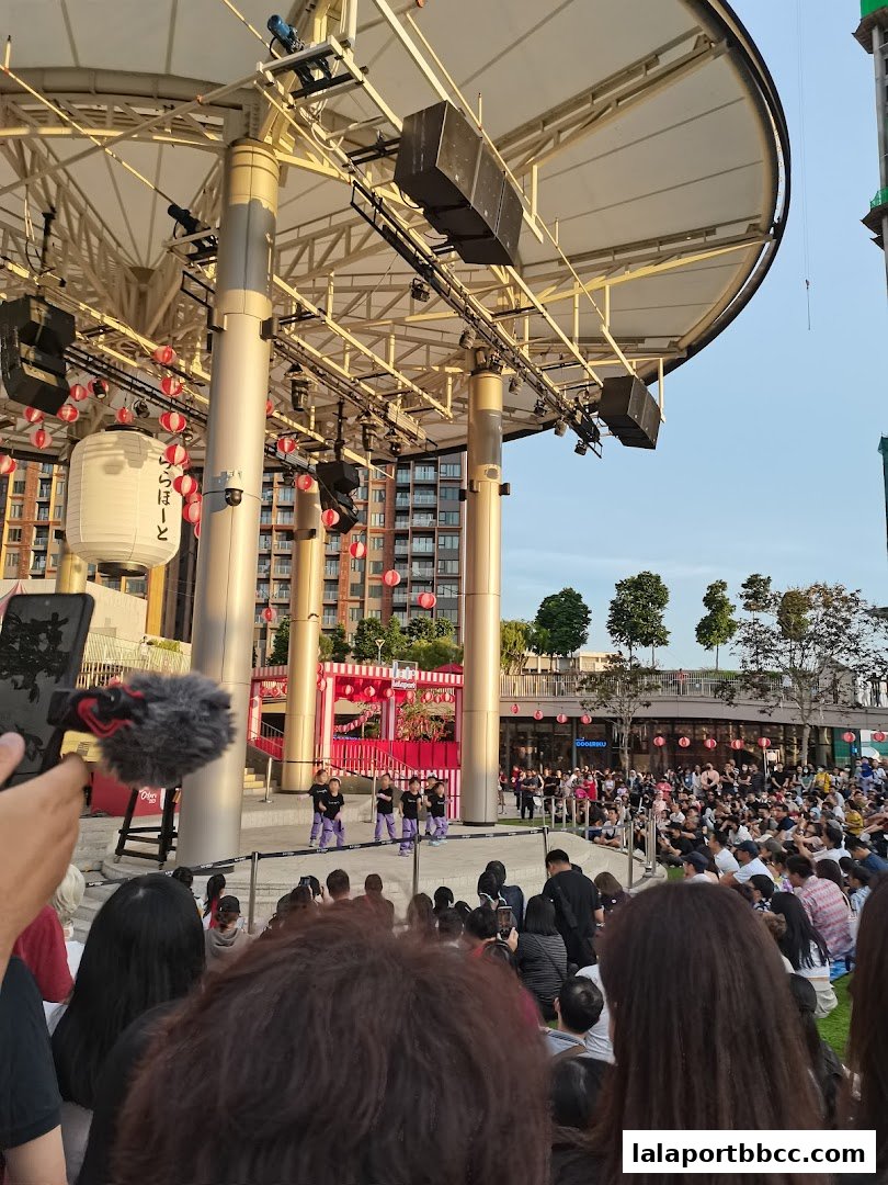 A crowd watches a performance on an outdoor stage decorated with lanterns.