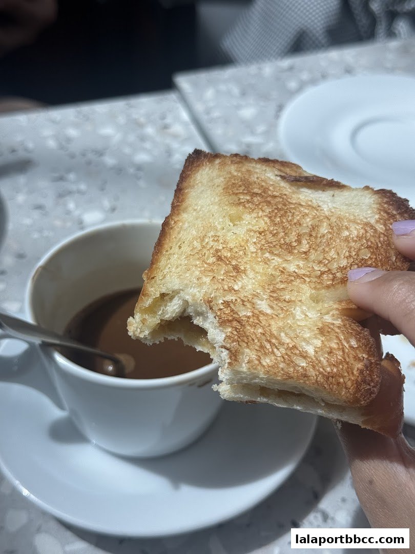 A person holds a bite of toast over a cup of hot chocolate.