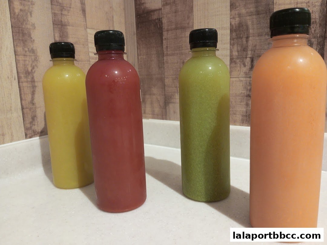 Four bottles of colorful juices are displayed on a counter.