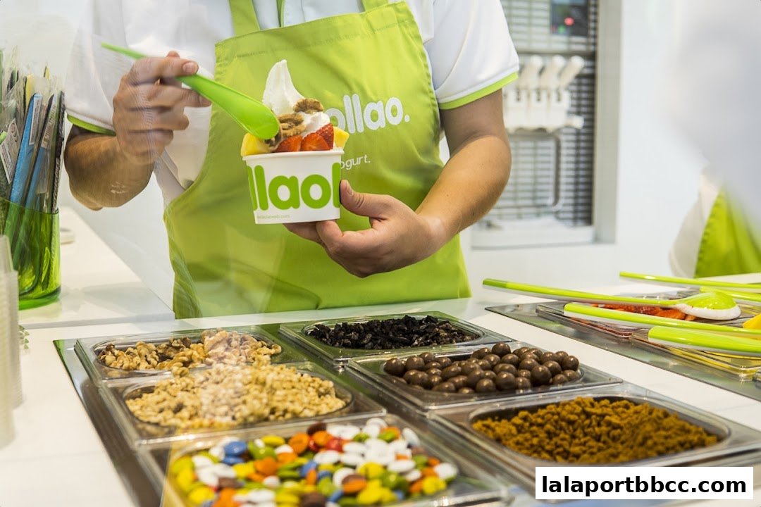 A person is preparing a frozen yogurt cup with various toppings like fruits and nuts.