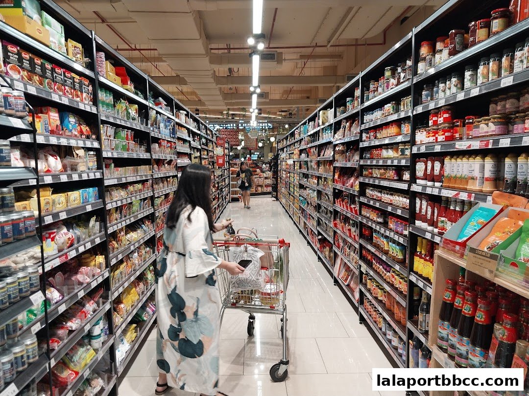 A shopper pushes a cart down a well-stocked grocery aisle with shelves full of products.