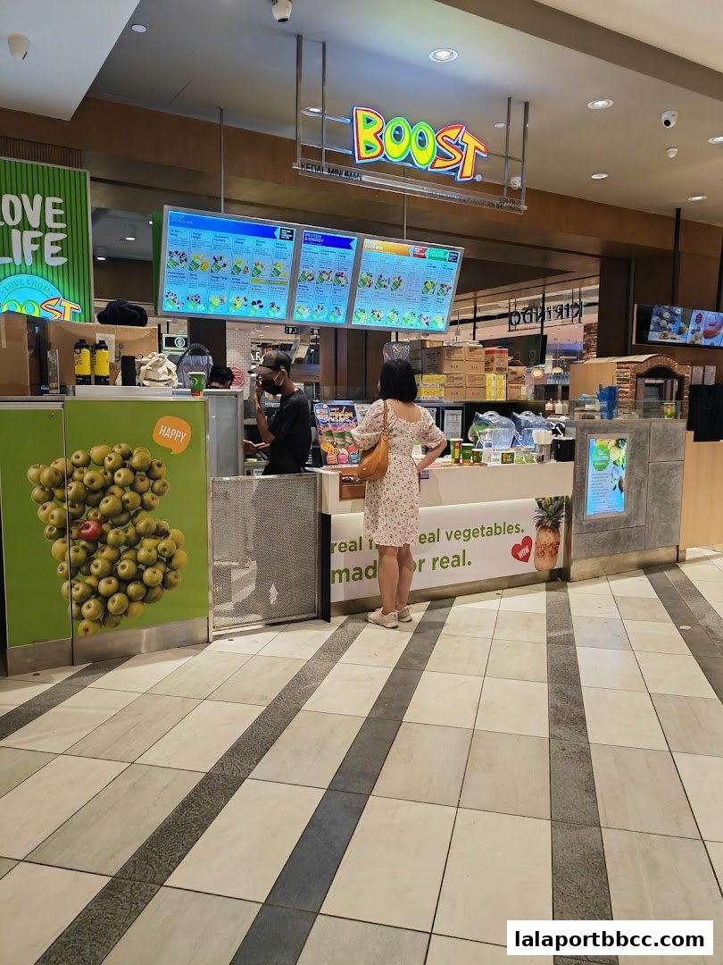 A customer orders at a Boost Juice counter with digital menus displaying colorful drinks.