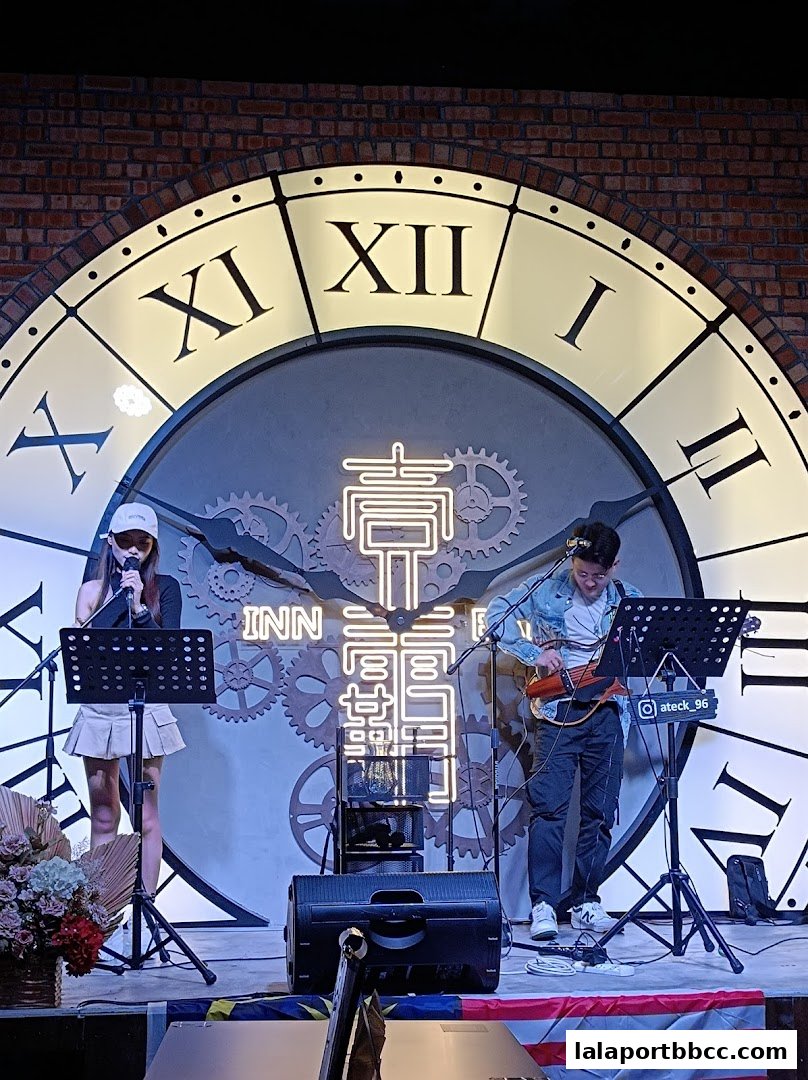 A live music performance with a singer and guitarist in front of a large clock.