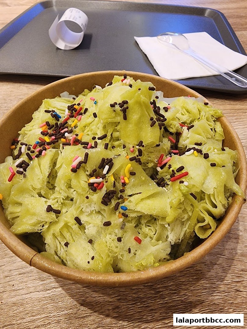 A close-up of a bowl of shaved ice dessert with green flavoring and colorful sprinkles.