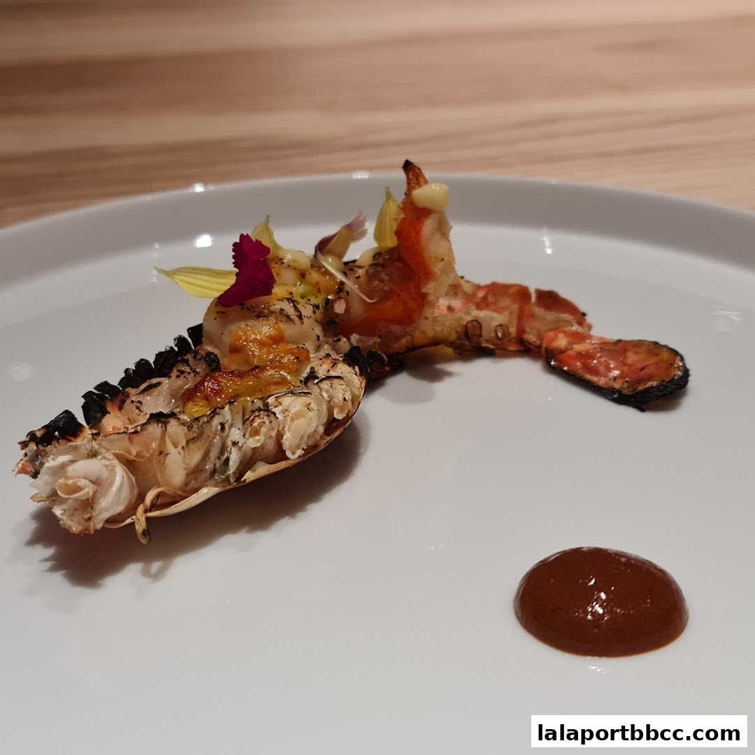 A beautifully plated grilled lobster tail with a side of sauce and edible flowers.