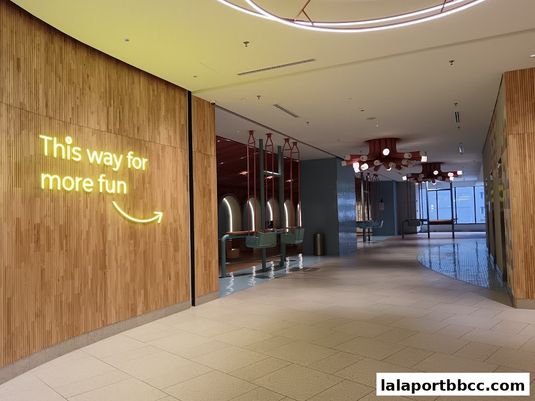 A modern interior hallway with a neon sign saying 'This way for more fun'.