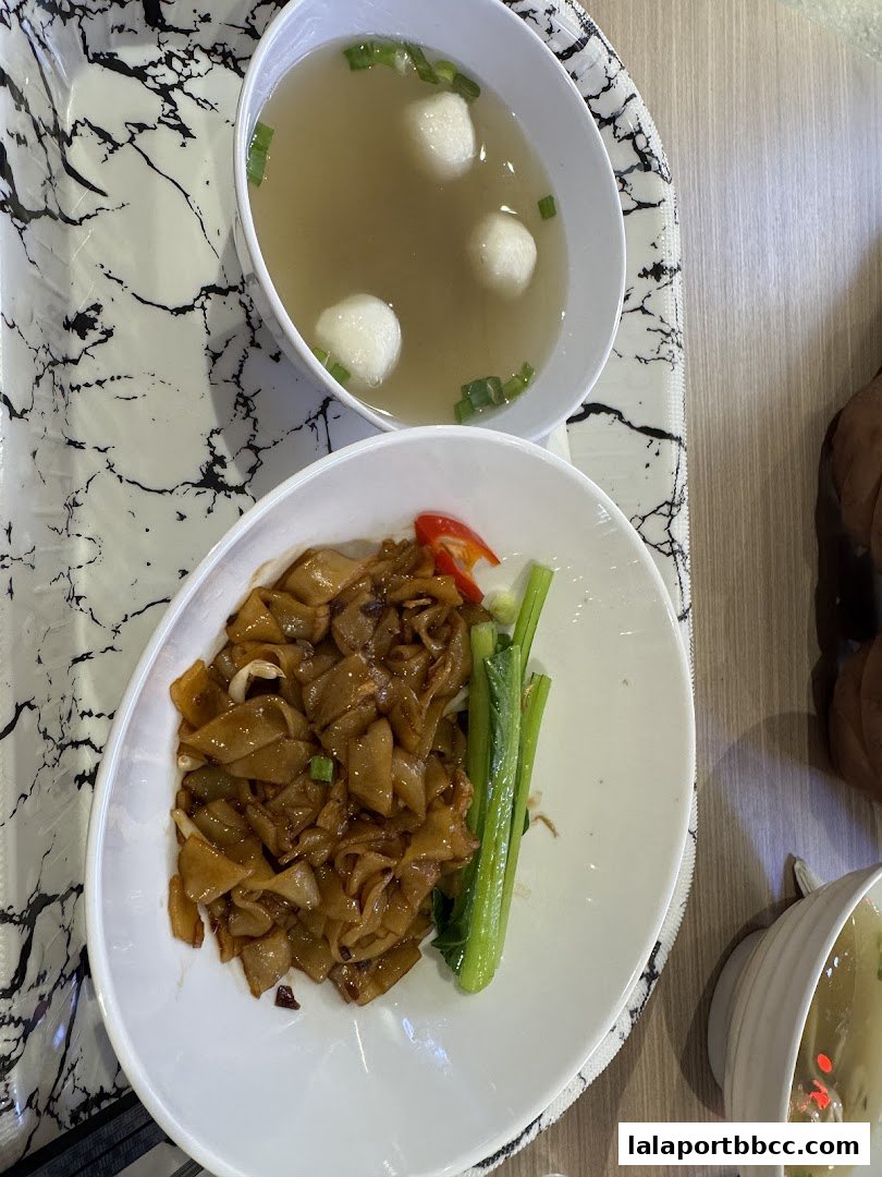 A close-up of a delicious plate of stir-fried noodles with a side of soup.