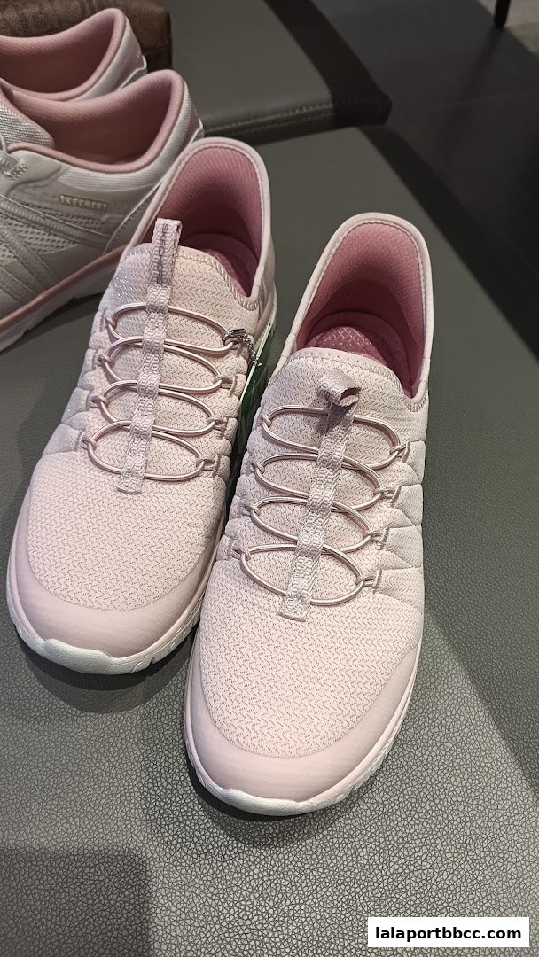 A pair of pink Skechers sneakers with elastic laces displayed on a textured surface.