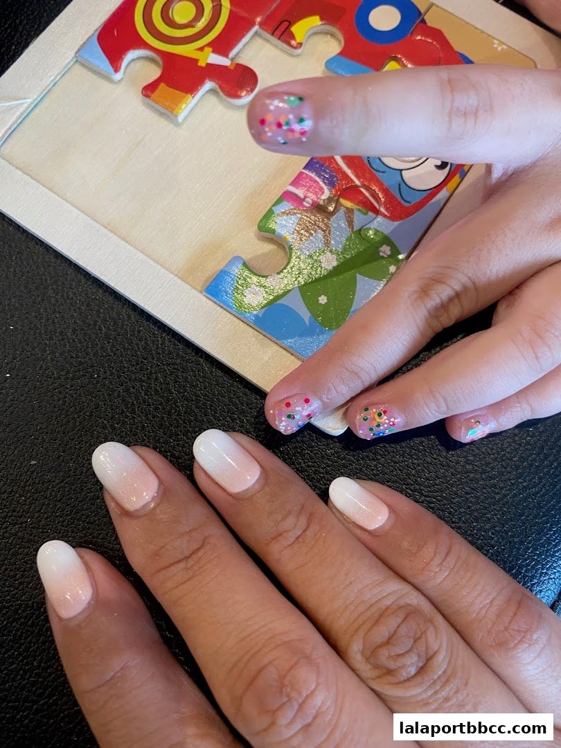 Close-up of hands with ombre and glitter manicures next to a colorful puzzle.