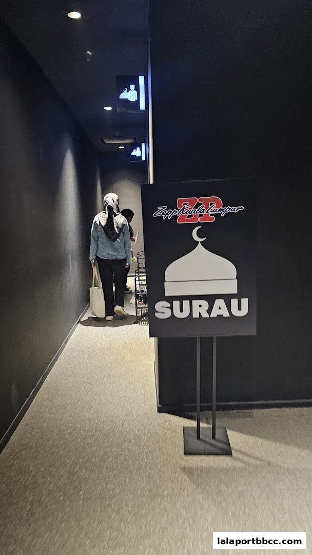 A sign for Surau at Zepp Kuala Lumpur with people walking by.
