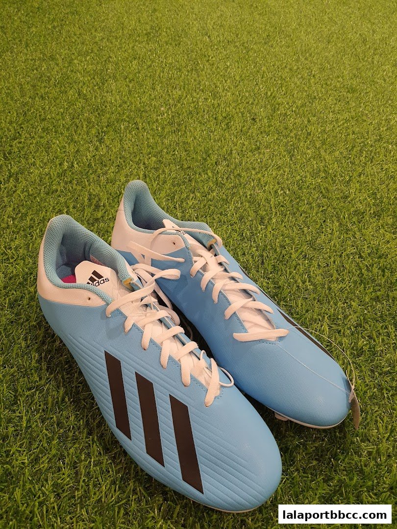 A pair of light blue Adidas soccer cleats with black stripes on a green grassy surface.