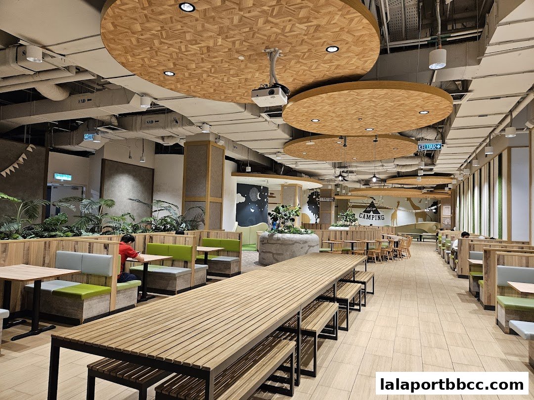 Interior of a spacious food court with wooden tables, benches, and green seating.