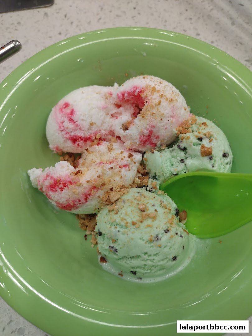 A bowl of ice cream with mint chocolate chip and strawberry swirl flavors, topped with nuts.