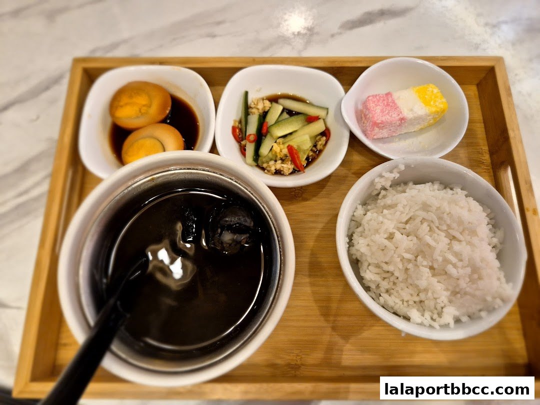 A tray of food featuring rice, braised eggs, pickled cucumbers, a dessert, and a dark beverage.
