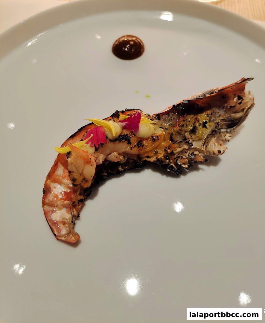 A beautifully plated grilled prawn dish with edible flowers and a sauce.
