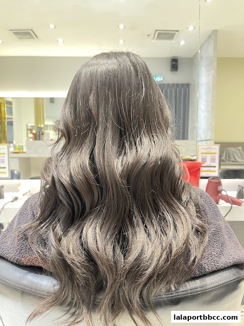A person with long, wavy, ash-brown hair sitting in a salon chair.