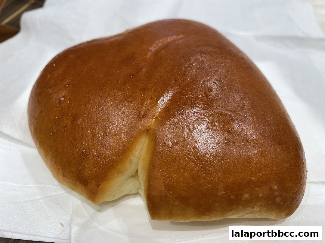 A close-up shot of a golden-brown, freshly baked bread roll on a white napkin.