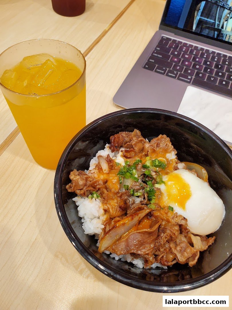 A bowl of beef rice with a soft-boiled egg and a glass of orange juice.