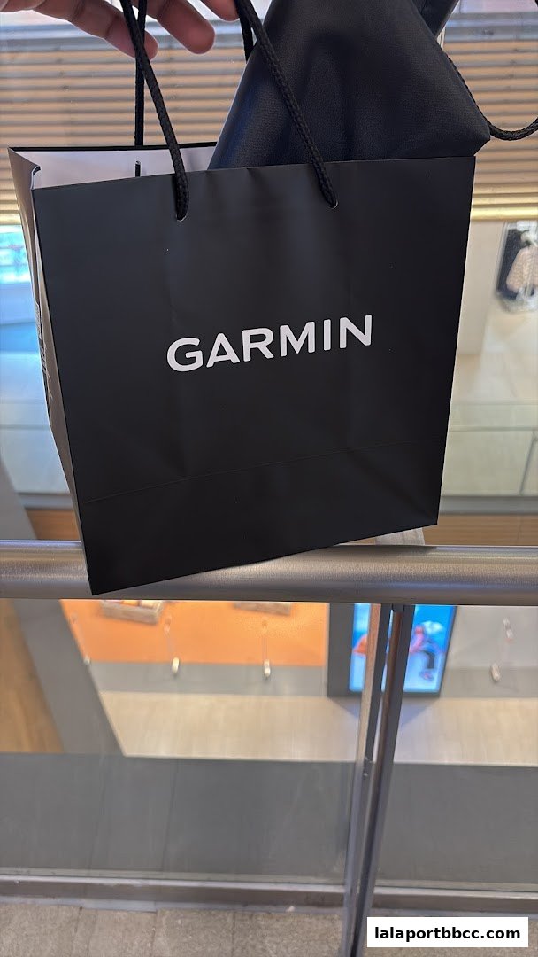 A hand holds a black Garmin shopping bag with a product inside.