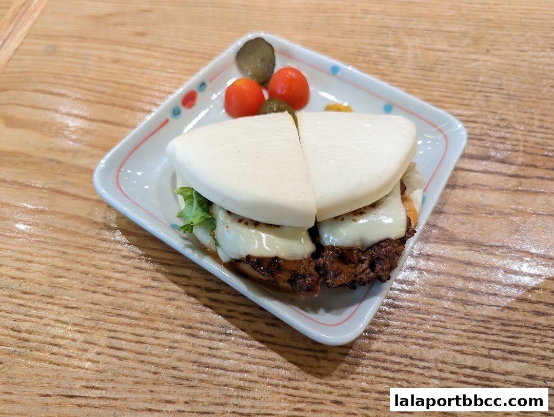 A delicious-looking bao bun burger with melted cheese and pickles on a decorative plate.