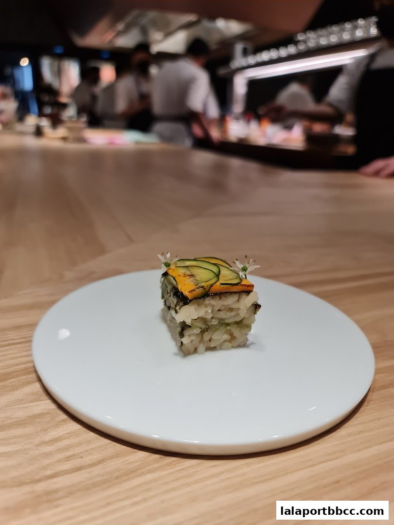 A meticulously prepared sushi dish with rice, vegetables, and edible flowers on a white plate.