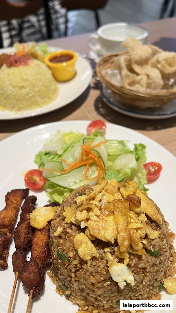 A close-up of two delicious meals, featuring fried rice, satay skewers, and a fresh salad.