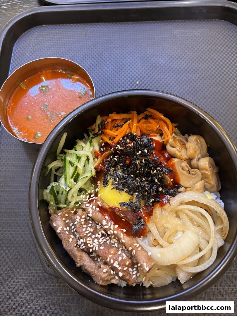 A delicious bowl of bibimbap with beef, vegetables, egg, and a side of sauce.