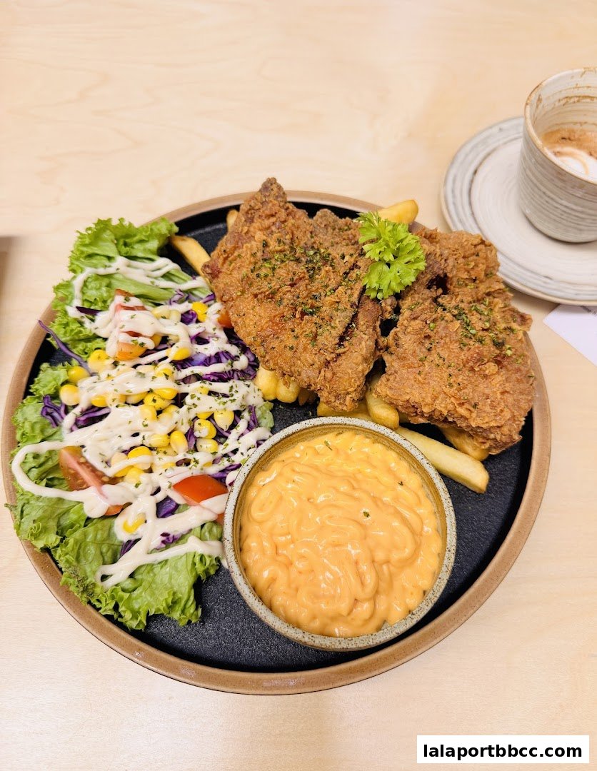 A plate of fried chicken with fries, salad, and a side of sauce, with a coffee in the background.