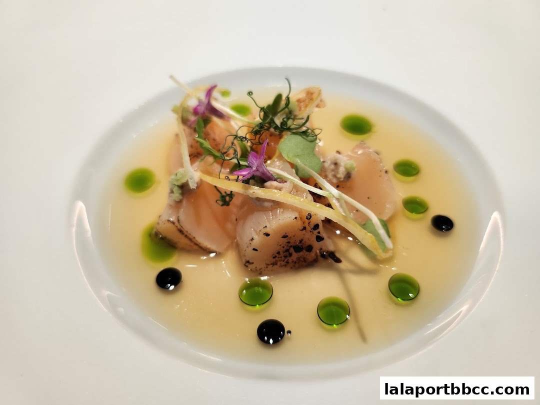 A beautifully plated dish of seared scallops and salmon in a clear broth with garnishes.