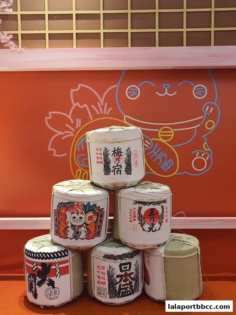 A stack of Japanese sake barrels with traditional designs and a Maneki-neko illustration.