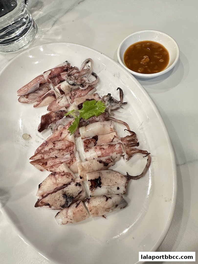 A plate of grilled squid served with a dipping sauce and a glass of water.