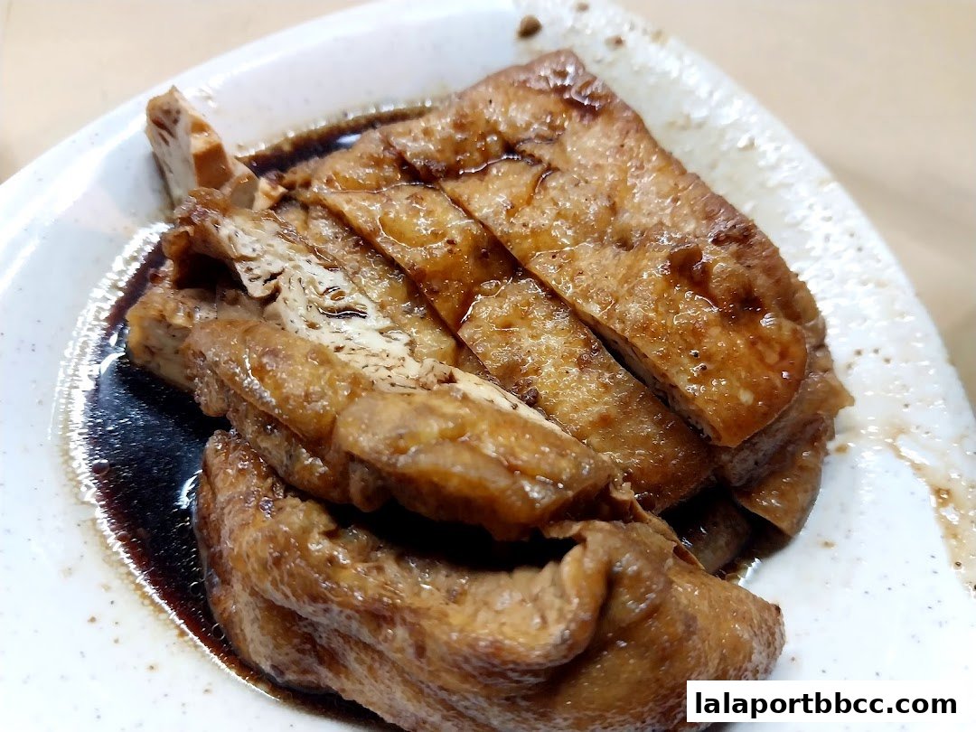 A close-up shot of braised tofu slices in a savory dark sauce on a white plate.